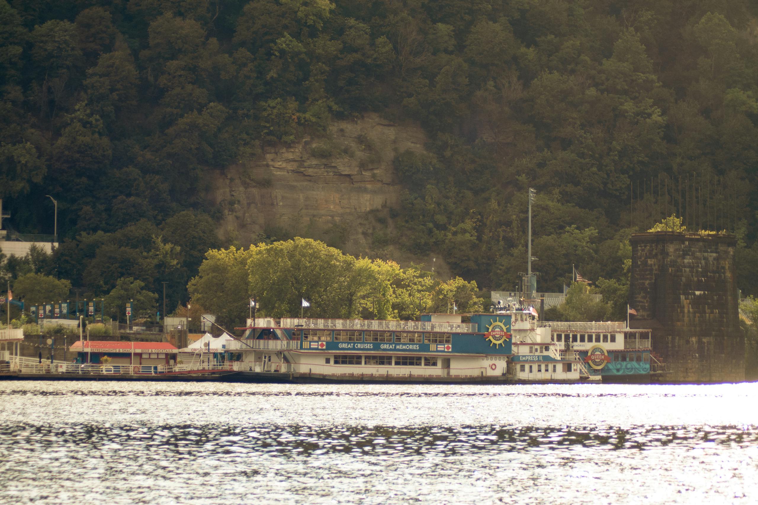 Classic riverboat docked by lush green cliffs in Pittsburgh, PA.